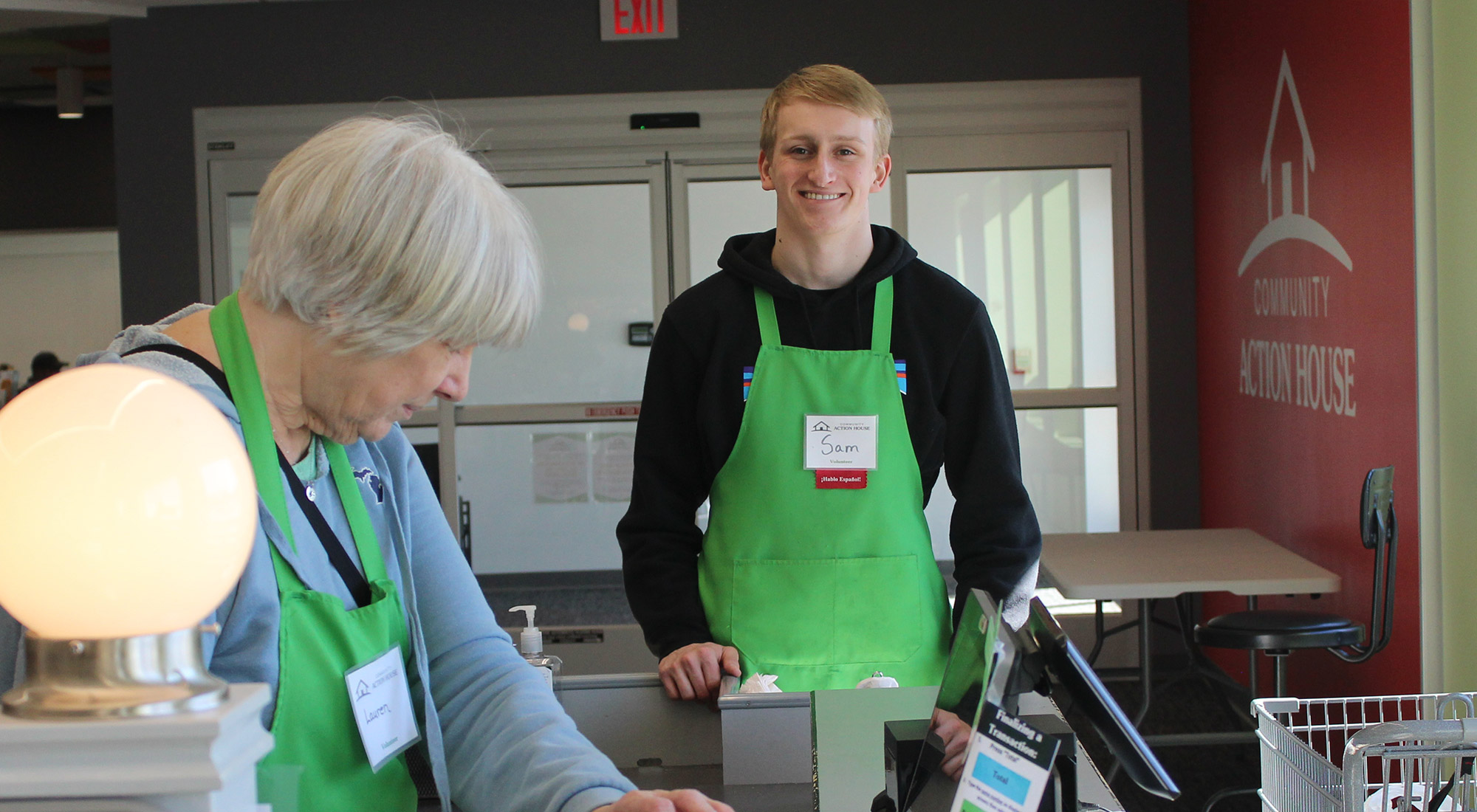 HCHS Spanish Immersion intern Sam working at Community Action House, waiting to bag groceries in his green apron, smiling