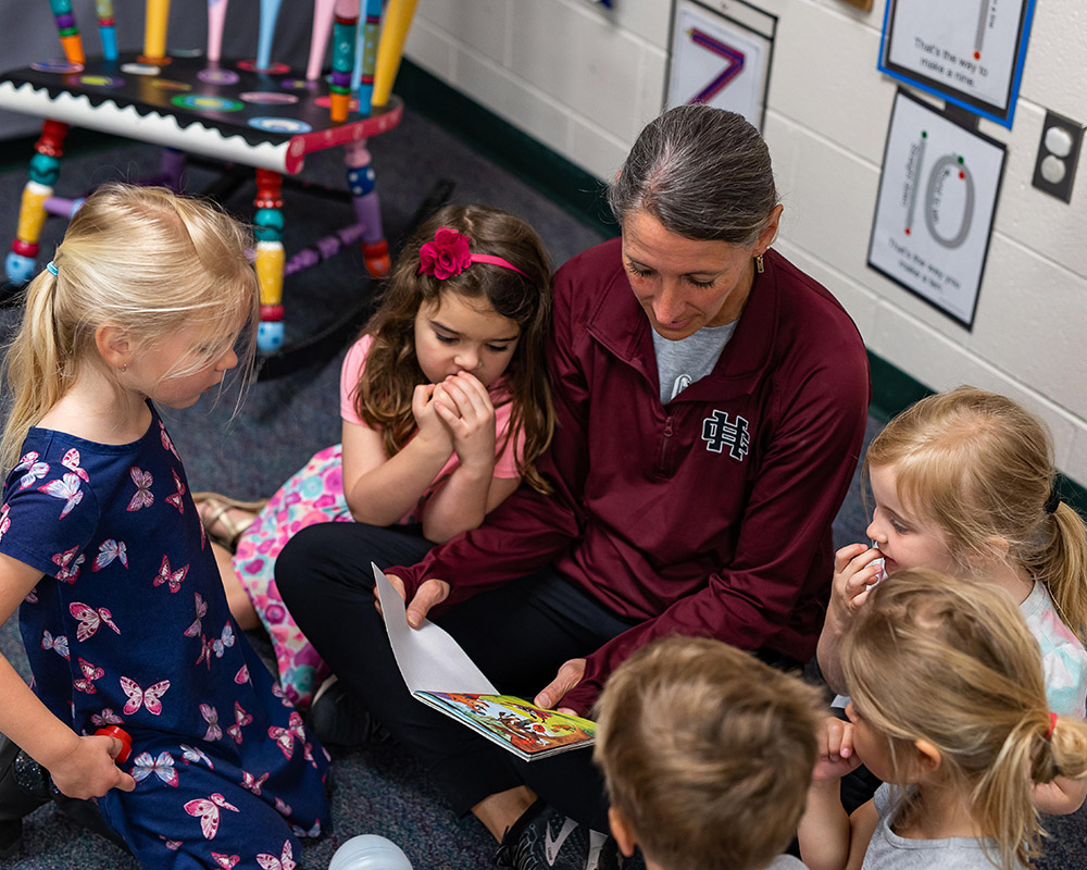 Preschool teacher reading to preschool students, sitting in a circle around the teacher