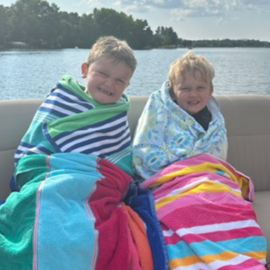 Two VanderWoude boys sitting on a boat and wrapped in beach towels