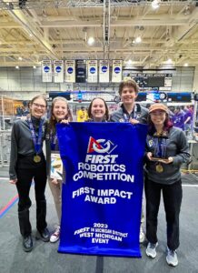 Members of the robotics team surrounding Nicki who is holding up a banner reading First Impact Award.