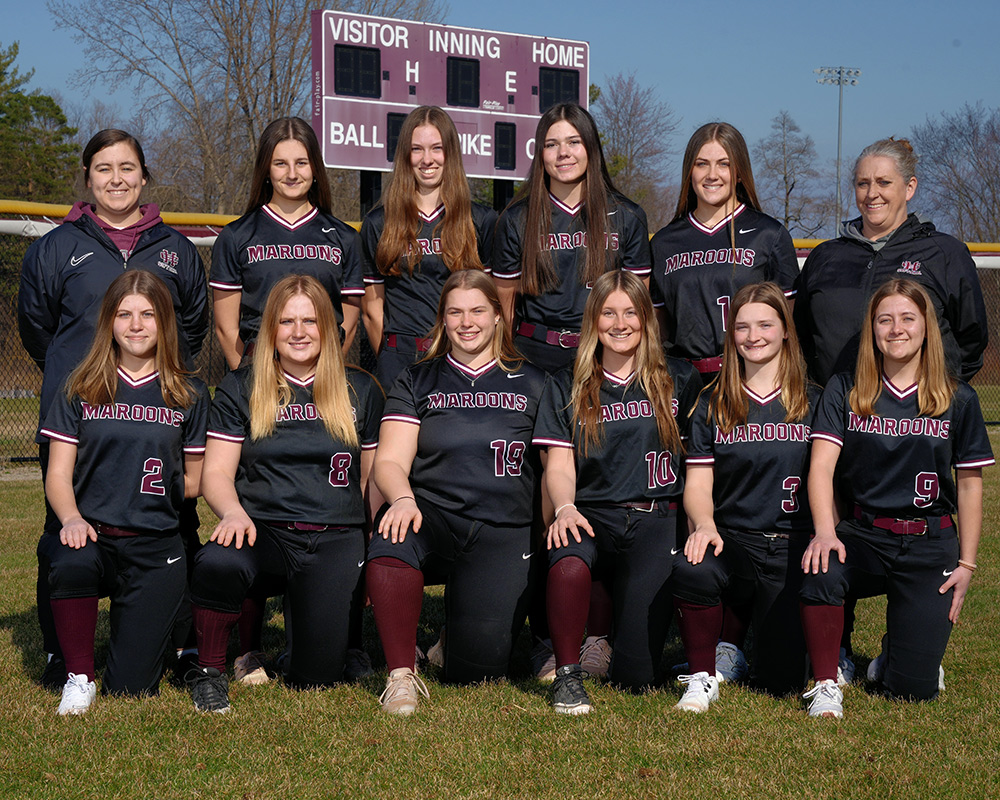 Varsity softball team in black uniforms, posing outside and smiling for the camera